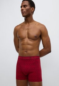 Κόκκινα μποξεράκια με σχέδια από μαλακό ύφασμα, με φαρδιά ελαστική μέση που φέρει τη φίρμα "BJÖRN BORG" και γεωμετρικά σχέδια.