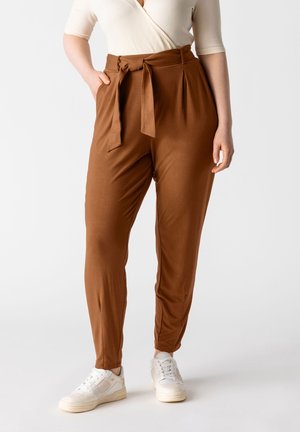 Bruine tapse broek met een tailleband met strik, zachte stof, plooien aan de voorkant en zijzakken, gecombineerd met witte sneaker.