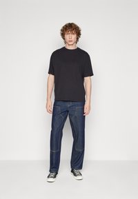 Black short-sleeve t-shirt paired with dark blue denim pants featuring visible stitching and a straight-leg design, worn with black sneakers.