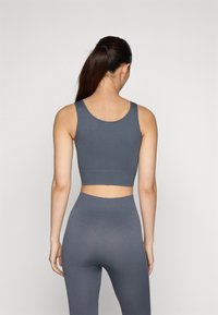 Grå, rillede trenings-BH med brede stropper, cropped passform, kombinert med matchende høyhånddekkende rillede tights, minimalistisk design, glatt tekstur.