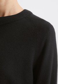 Μαύρο πουλόβερ με στρογγυλή λαιμόκοψη, πλεκτή υφή και χωρίς ραφές. Ελαφρώς ελαστικό ύφασμα με λεία φινίρισμα.