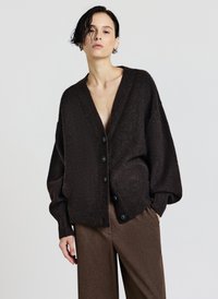 Brauner gestrickter Cardigan mit tiefem V-Ausschnitt, oversized Passform und fünf dunklen Knöpfen. Verfügt über gerippte Ärmel und einen weichen Stoff. Kombiniert mit brauner Hose.