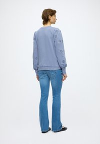 Svjetloplavi pulover s nabranim rukavima i sitnim cvjetnim izrezima. Kombiniran s plavim trapezasto širokim trapericama i crnim sandalama.