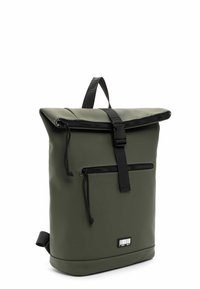 Sac à dos à rabat vert en matériau imperméable, avec une poche zippée à l'avant, des bretelles noires et un design minimaliste sans logos visibles.