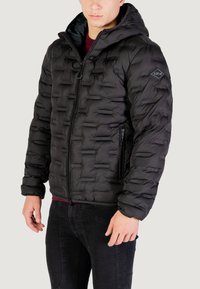 Giacca a vento nera con cappuccio, caratterizzata da un design trapuntato, chiusura con zip e tasche laterali. Realizzata in tessuto lucido e liscio.
