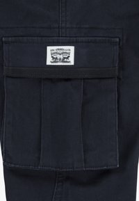 Pantaloni cargo in denim nero con una grande tasca a toppa con etichetta bianca Levi Strauss & Co. e dettagli in tessuto testurizzato.