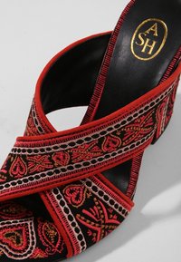Sandale à talons noire avec motifs brodés géométriques et floraux en rouge, rose et or, disposés en croisillons, avec logo doré "ASH" à l'intérieur.