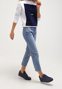 Vit och marinblå sweatshirt med en fyrkantig marinblå panel, ljusblå jeans och mörkblå sneakers. Sneakers har texturerad yta och låg profil.