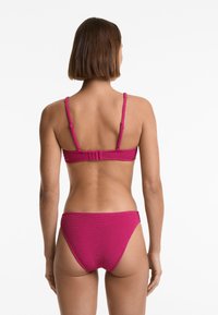 Magenta bikiny s texturovanou látkou, s tenkými nastavitelnými ramínky a sponou na zádech. Spodní díl má vysoký střih na nohavičkách.