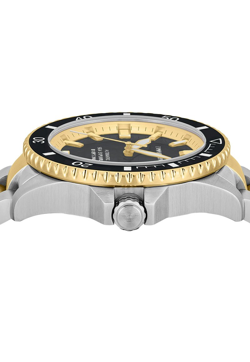 Rund klocka i rostfritt stål med en guldkant, svart urtavla, gyllene timmarkörer och ett texturerat silverarmband. Har en krona på sidan.