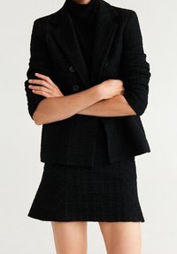 Ensemble blazer et jupe noir sur mesure, tissu texturé, design croisé à double boutonnage, boutons ronds, coupe ajustée, et jupe courte évasée.