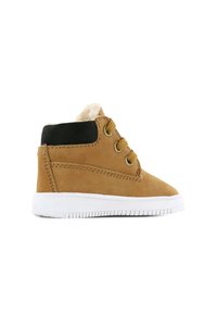 Bruine leren enkellaars met witte rubberen zool, ronde neus, gouden veterogen en zwarte accenten op de hak. Voering van licht bont.