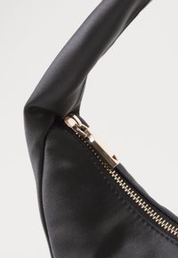 Svart satinhåndveske med glatt tekstur, med glidelås i gulltone og polert maskinvare langs kanten av vesken.