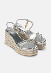 Sandalias de cuña plateadas con tiras cruzadas brillantes, acabado metálico, plataforma de yute trenzado y suela de color bronceado texturizada.