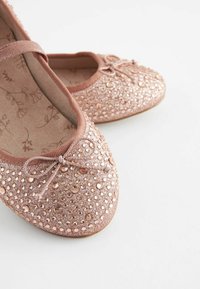 Bailarinas en rosa empolvado con un upper de tela texturizada, decoradas con lentejuelas redondas que atrapan la luz y un lazo decorativo en la punta.