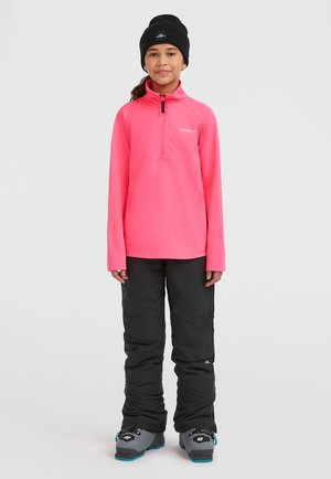 Fuchsia mellemlagstop med lynlås i halsen, parret med sorte isolerede bukser og grå skistøvler med blå accenter. Sort hue fuldender looket.