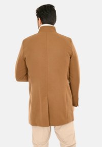 Cappotto marrone strutturato con spacco singolo sul retro, realizzato in tessuto liscio. Presenta un colletto alto e maniche lunghe.