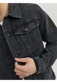 Black denim jacket with a button-up design, chest pockets, and a textured finish. Features a classic collar and slightly distressed details.