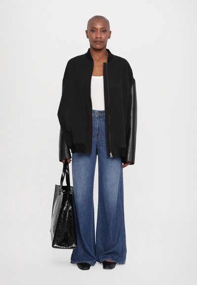 Oversized black bomber jacket with leather sleeves, white tank top, wide-leg blue jeans, and a glossy black tote bag.