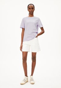 Hellblaues Kurzarm-T-Shirt kombiniert mit weißen Baumwollshorts. Das Model trägt weiße, gewebte Sneakers mit strukturierter Oberfläche.