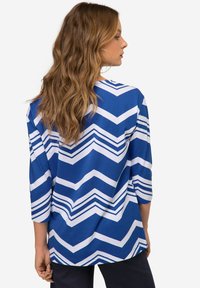 Niebieska i biała koszula w wzór zygzaka z rękawami o długości trzech czwartych i zaokrąglonym dołem, wykonana z miękkiej, lekkiej tkaniny.