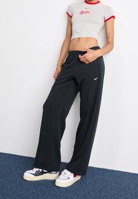 Gray crop top with red accents, featuring a front logo. Black wide-leg sweatpants paired with white and red shoes. Smooth textures throughout.