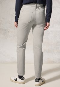 Pantaloni di cotone grigio chiaro con taglio dritto, con tasche laterali e posteriori visibili, indossati con sneakers bianche con dettagli neri.