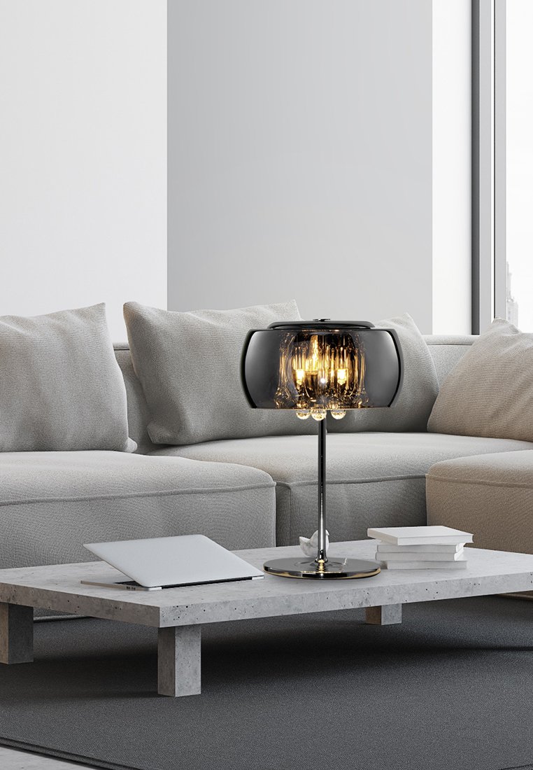 Svart glaskupa lampa med en rund skärm, metallbas och synliga glödlampor. Står på ett grått betongkaffebord med vita böcker.