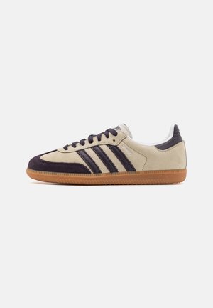 Beżowy i ciemnobrązowy sneaker Adidas Samba z gumową podeszwą, bocznymi paskami i sznurowanym fasonem, widoczny od strony zewnętrznej na białym tle.