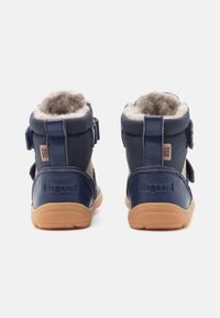 Bottines en cuir bleu marine avec une doublure en fourrure marron douce, deux bandes Velcro réglables et une semelle en caoutchouc texturée. Nom de la marque embossé sur le talon.