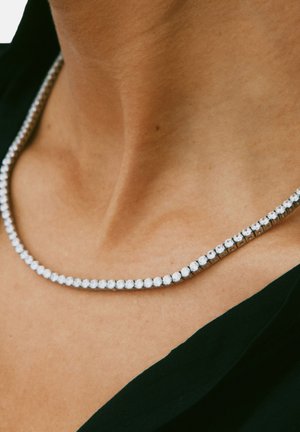 Collana di strass con un design flessibile, con pietre trasparenti incastonate in una catena di metallo tono argento, posata sulla pelle nuda.