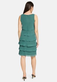 Robe en chiffon bleu sarcelle avec un design sans manches, des volants superposés et une fermeture éclair au dos. L'ourlet tombe au-dessus du genou.