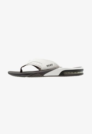 Tongs blanches et noires avec une tige texturée, des perforations et une semelle rembourrée présentant un coussin d'air visible pour le confort et le soutien.