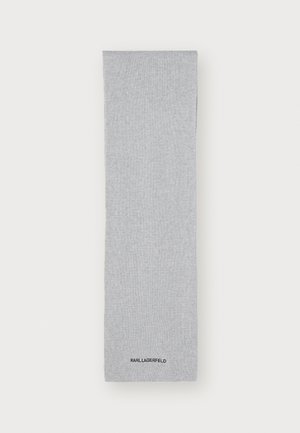 Pelēki ribotie kāju sildītāji, izgatavoti no mīksta materiāla, ar smalku tekstūru un melnu logotipu apakšā.