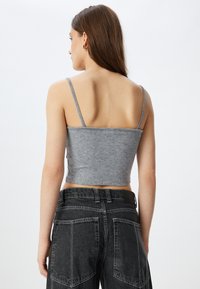Top ajustado gris con tirantes finos, hecho de una tela suave; combinado con pantalones de mezclilla negros de tiro alto con grandes bolsillos traseros.