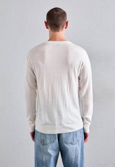 Hellbeige langärmliger Pullover mit geripptem Kragen und Bündchen, kombiniert mit lockeren hellblauen Jeans. Weiche, glatte Textur.