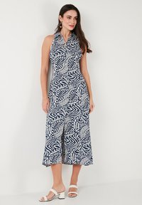 Navy blue halter dress with white leaf-patterned design, featuring a button-down front and a flared hem. Fabric has a smooth texture.