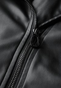 Tissu en simili cuir noir avec une fermeture éclair bien visible. Surface texturée, couture visible le long de la couture, et un détail de tirette de fermeture éclair élégant.