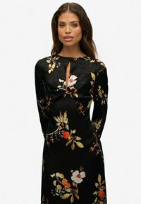 Czarna sukienka w kwiaty z długimi rękawami, z wycięciem w kształcie łezki i gładką fakturą. Kwiatowe wzory w kolorach białym, pomarańczowym i żółtym.