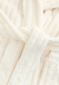 Peignoir en peluche couleur crème avec une surface douce et texturée, doté d'une fermeture à nouer et d'un motif subtil à rayures verticales.