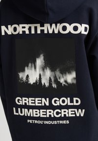 Felpa blu marina con grafica in bianco e nero raffigurante alberi, testo in grassetto che recita "NORTHWOOD", "GREEN GOLD LUMBERCREW" e "PETROL® INDUSTRIES."