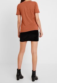 Rustfärgad bomull t-shirt med korta ärmar, ihopparad med en svart denim minikjol och svarta ankelstövlar. Enkel design, utan mönster.