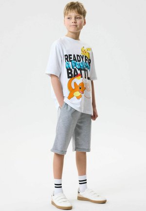Blond boy wearing grey shorts, white socks with black stripes, white sneakers, and a Pokemon T-shirt featuring Pikachu and Charmander.