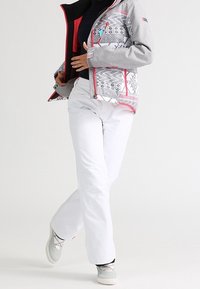 Grau gemusterte Jacke mit pinken Akzenten, weiße Skihosen und graue Stiefel. Die Jacke weist geometrische Designs und ein kontrastierendes Innenfutter auf.