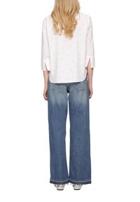 Chemise blanche avec un petit motif de cœurs roses, à manches 3/4 et fentes sur les côtés, assortie à un jean bleu clair à jambes larges avec des bords effilochés.