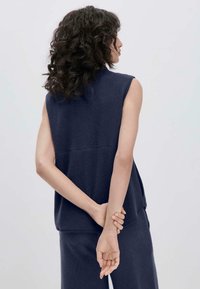 Ärmelloses navy-farbenes Fleece-Oberteil mit entspannter Passform, weicher Textur und hohem Kragen, kombiniert mit passenden Hosen, sieht von hinten aus.