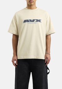 Beżowy bawełniany t-shirt z krótkim rękawem, z niebieskim haftowanym logo "AVX" oraz napisem "AVIREX DEPT." z przodu. Prosty krój.
