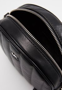 Borsa a tracolla nera in pelle con zip argentata parzialmente aperta, motivo trapuntato e piccolo logo metallico sulla parte anteriore.