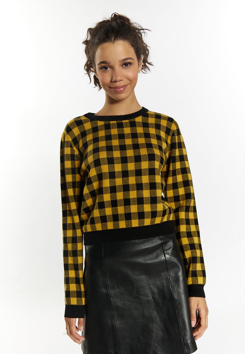 Maglione giallo e nero a scacchi con maniche lunghe, colletto rotondo e orlo a costine nero, abbinato a una gonna in pelle nera.