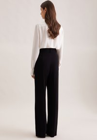 Czarne szerokie spodnie o dopasowanym kroju, wysoki stan i gładka tekstura. W zestawieniu z białą bluzką z długim rękawem z guziczkami przy mankietach.